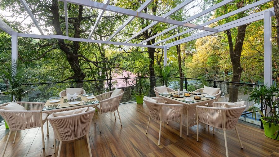 The deck at DLS The Emerald, Nainital with chairs and tables with the background of trees and greenery