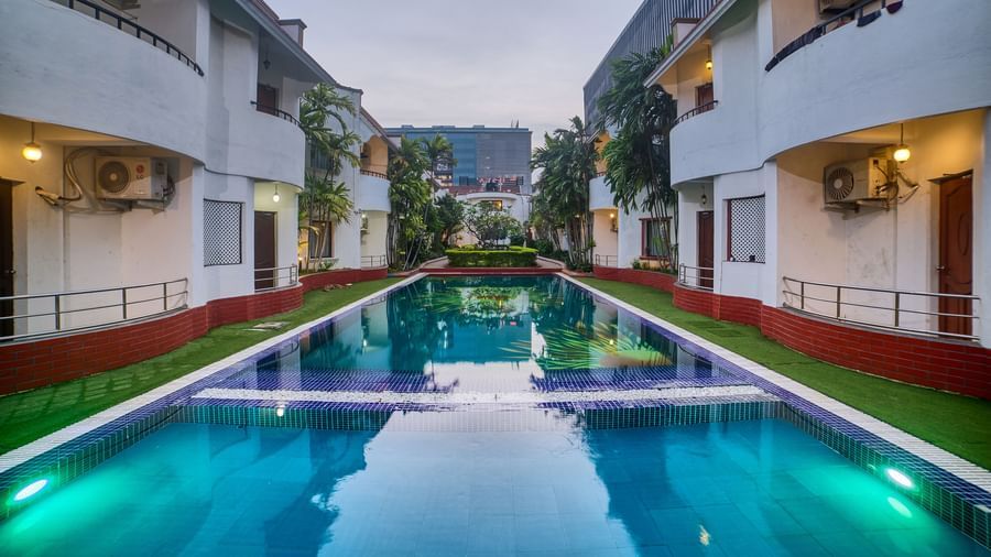 A symmetrical view of Ilara Hotels & Spa, OMR, Chennai illuminated at dusk, lining a long, reflective swimming pool or water feature.