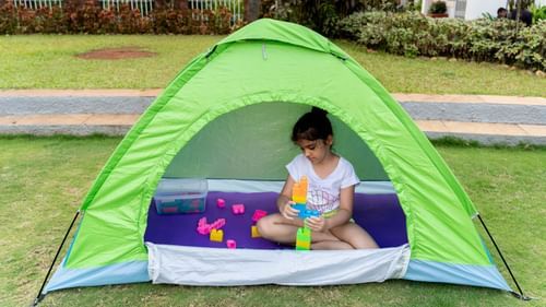 A kid playing with building blocks inside a tent placed on the lawn
