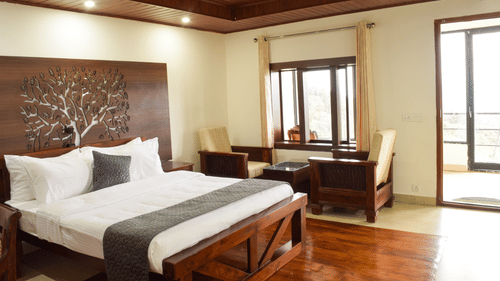 A side angle shot of the premium room featuring a king size bed, a seating area with two couches and a table  and a private balcony | A side angle shot of the suite at the resort feature a expansive balcony that overlooks the lush green valleys, king size 