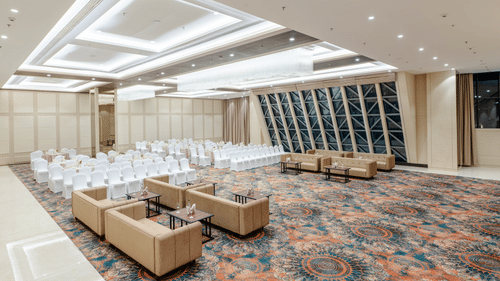 A wide angle shot of a banquet hall in ajmer featuring cosy seating arrangement, high ceilings, and bright lighting - Sarovar Portico, Ajmer