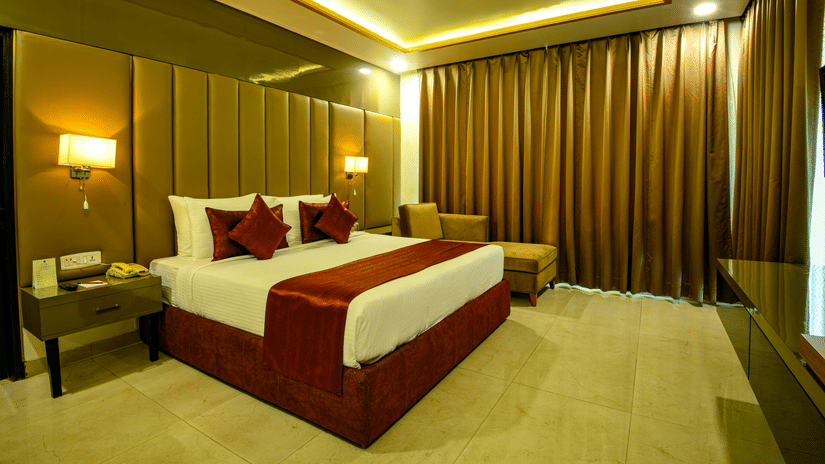 Hotel room at Hotel Kanha Shyam, Prayagraj, with a king-sized bed, warm lighting and a mirrored feature wall.