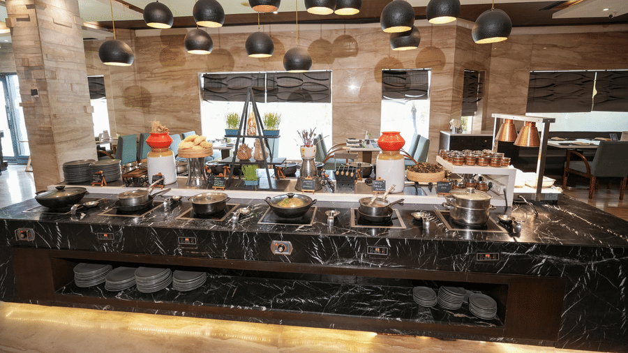 A buffet counter at Park Plaza Ludhiana featuring a dark marble surface with food displays hanging pendant lights and a stone textured wall backdrop in a warmly lit setting.