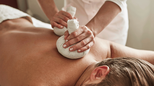 A person lying on their stomach and a couple of hands using poultices on their bare upper back