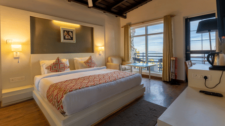 Large suite bedroom with a double bed, bedside lamps, and a glass door leading to a balcony at Himalayas Resort By The Lake Hill, Mukteshwar.