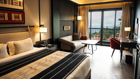 Bedroom with king bed, sofa, writing desk, wall art, and glass sliding door opening to scenic balcony views.