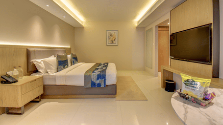 A well-lit Deluxe King room at The SSK Solitaire Boutique Hotel & Spa, Gangapur Road - Nashik featuring a king size  bed, two armchairs, a small table, and a work desk with a chair.