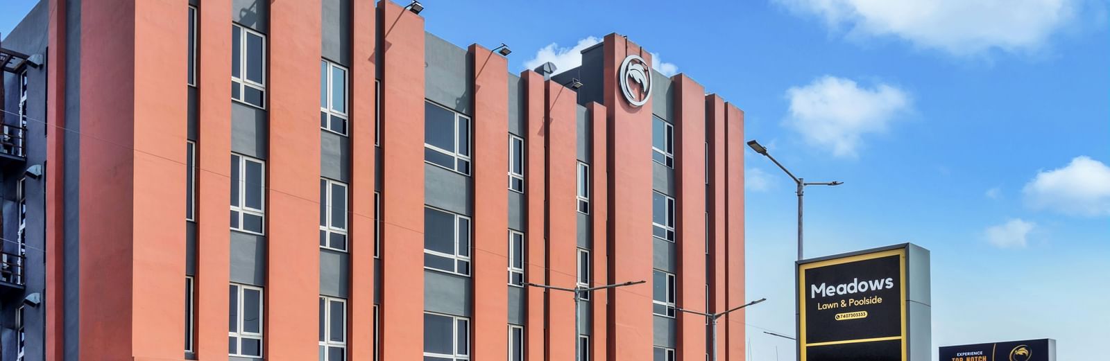 A modern, multi-story hotel building with orange and grey facade under a blue sky with scattered clouds  | The Citi Residenci Hotel Banskopa