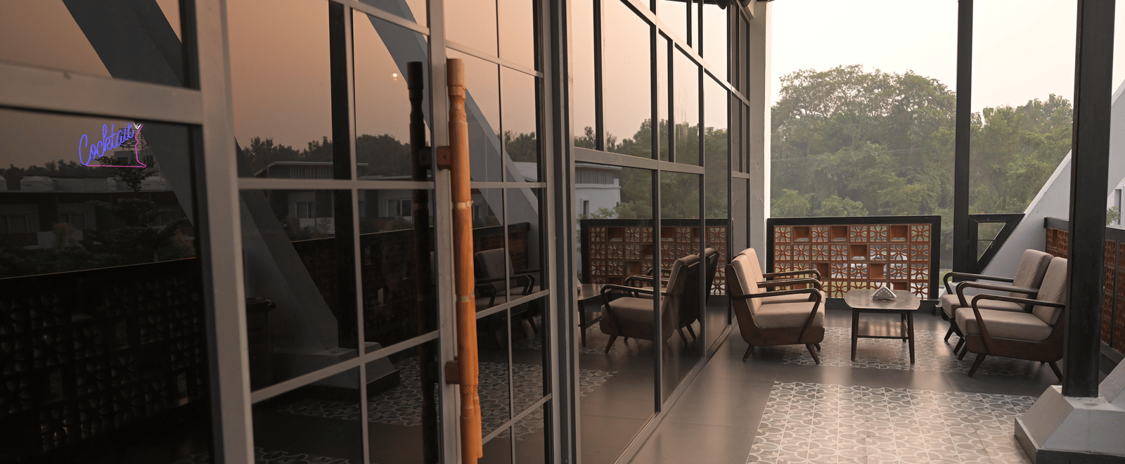 Glass doors opening into a stylish outdoor lounge with patterned flooring and sunset reflections at Hotel Sonar Bangla Mayapur.