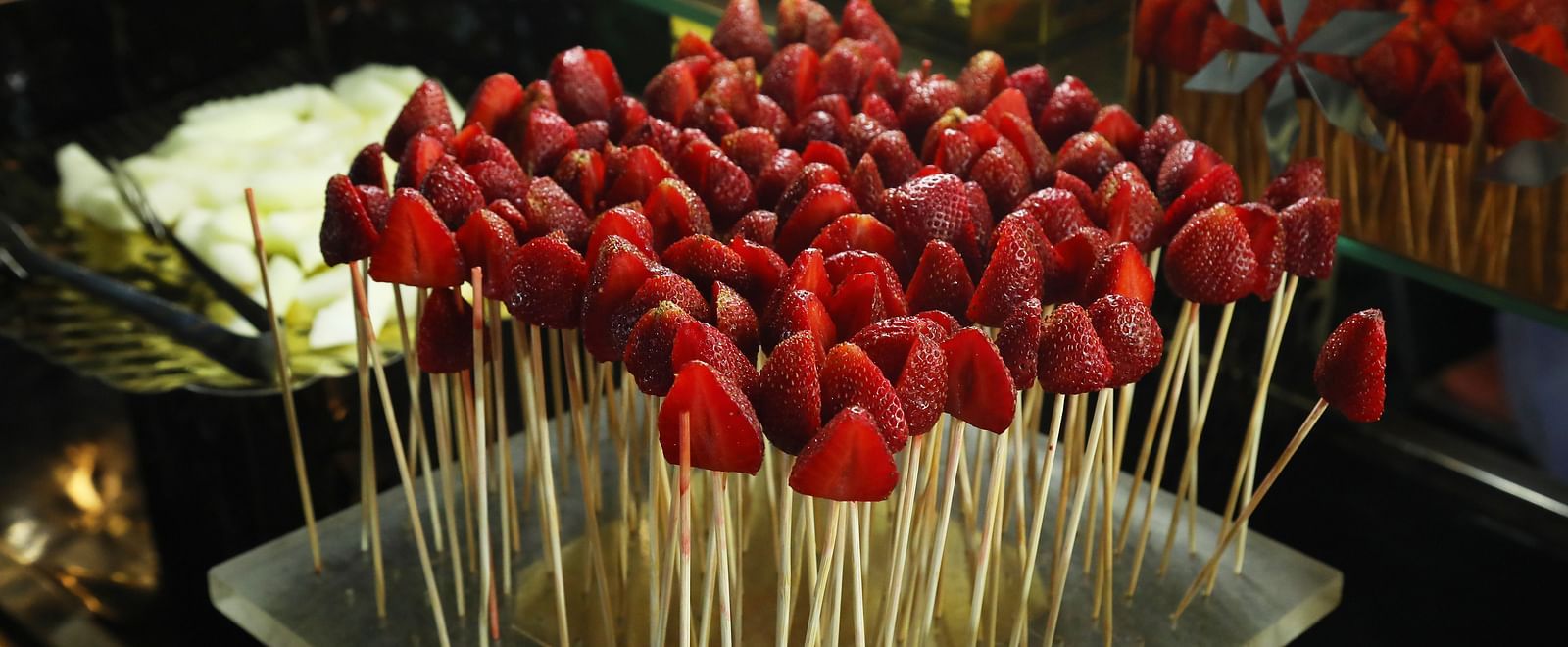 Food display at Tisya Farms, Gurgaon showing skewers of strawberries and grapes on a black tray.