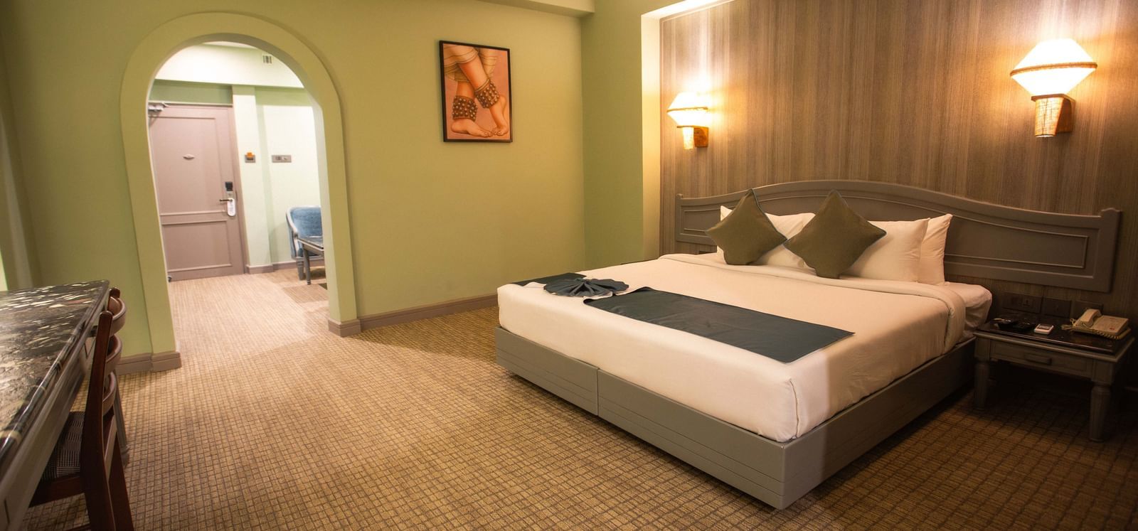  A guest room at Shilton International, Kochi, with a bed, a desk, and an arched doorway leading to another area.
