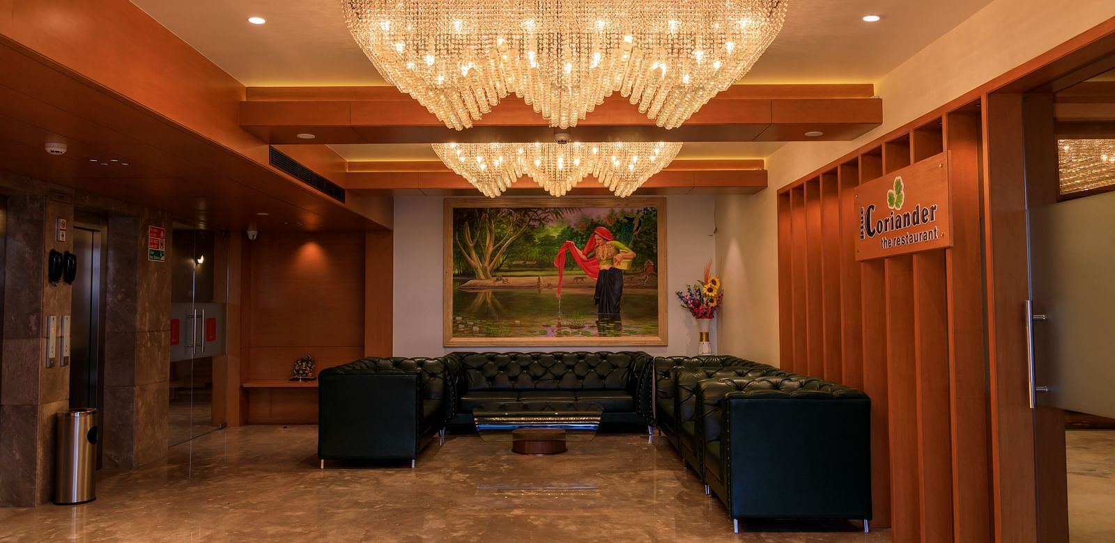The warmly lit lobby of Lords Eco Inn Apple Gate features plush seating, artwork, distinctive chandeliers, and lift access.