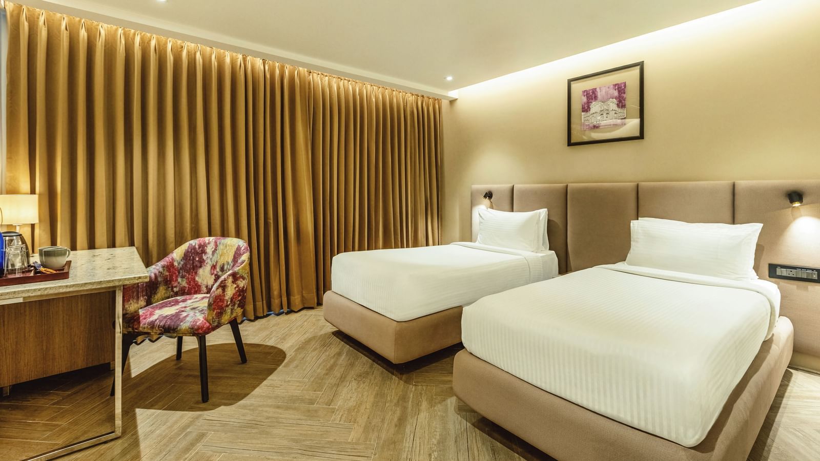 A wide shot of a twin-bedded room at Mango Hill Central, Chennai. A desk is on the left, and a wooden slat wall is behind the beds.