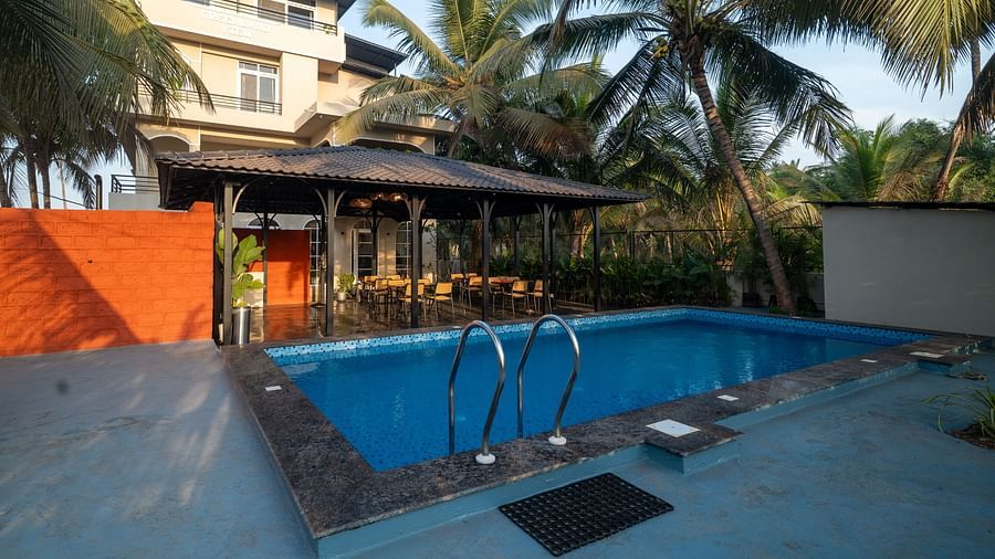 Outdoor swimming pool surrounded by palm trees, adjacent to a covered open-air seating area and Kseemya in the background.
