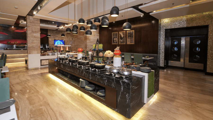 A restaurant bar area at Park Plaza Ludhiana featuring a long counter with pendant lights wooden flooring track lighting on the ceiling and colorful decor in the background.