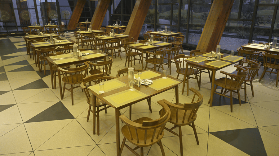 A high-angle view of rows of wooden dining tables with yellow placemats at Hotel Sonar Bangla, Mayapur.