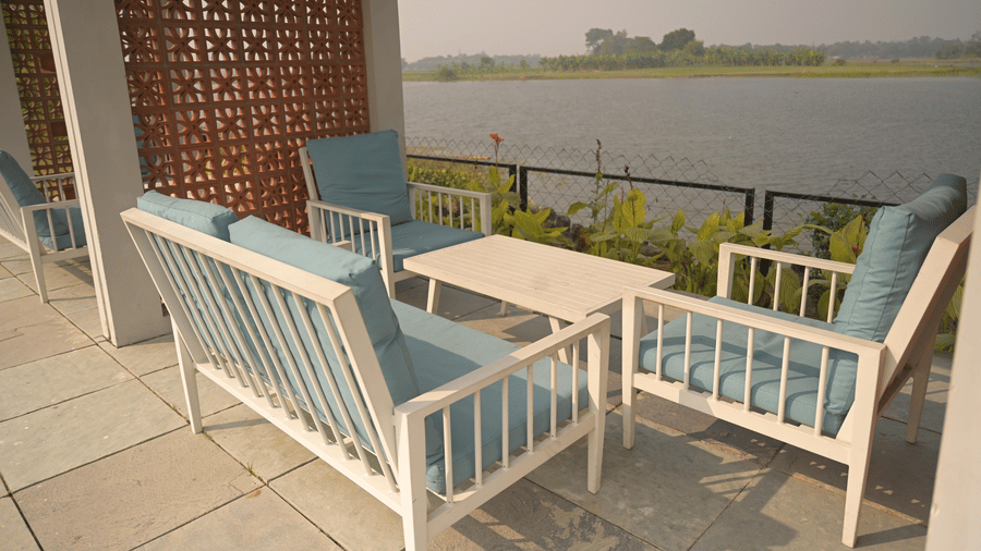 Riverside patio seating with cushioned chairs and a view of the water at Hotel Sonar Bangla, Mayapur.