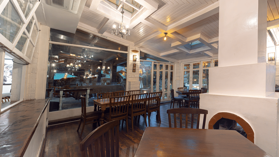 An indoor restaurant space with dark wood tables, white-painted pillars, and warm overhead lighting - Johnson Lodge & Spa, Manali