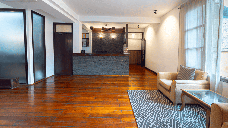 A clean, minimalist lobby area with polished wooden floors, a simple reception desk, and a cozy armchair seating nook - Johnson Lodge & Spa, Manali