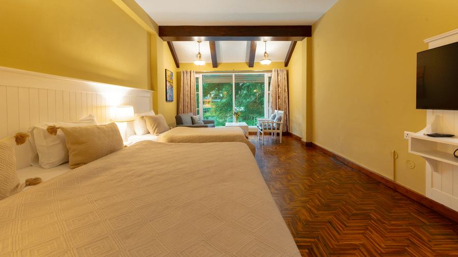 A large guest room with warm yellow walls, dark wood ceiling beams, and parquet flooring - Johnson Lodge & Spa, Manali