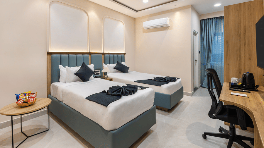 2 single beds with white bedding, a desk with an office chair, and a ceiling fan, at Monday Hotels & Suites Madhapur Hyderabad.