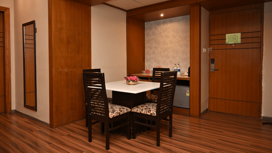 Suite dining area with a wooden dining table and chairs, wood-panelled walls, warm lighting and dark wooden flooring throughout the space.