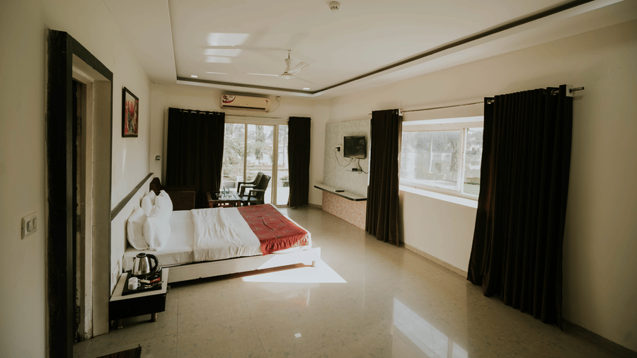 A bedroom at TGI Jahaj Mahal, Mandu, with a king size bed with white sheets, air-conditioning, and side tables.