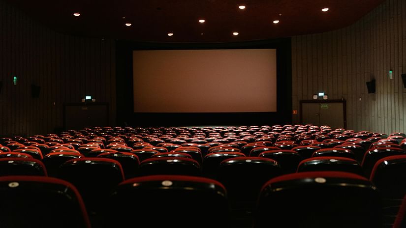 An empty theatre with rows of red seats facing a large movie screen.