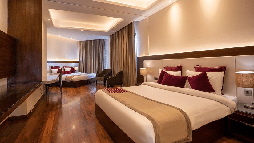 Room at Marigold Sarovar Portico, Mashobra Shimla, with a wooden bed, red cushions, a seating nook, wall mounted television and polished wooden flooring.
