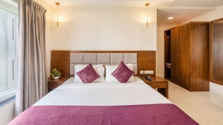 A well-lit room at Destino by Monday Hotels, Gachibowli, featuring a neatly made double bed with purple accents and a spacious wooden wardrobe.