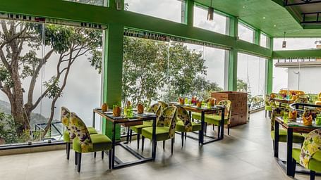 An image of a restaurant with seating arrangement and expansive glass window over looking the serene mountains - Great Trails Yercaud by GRT Hotels