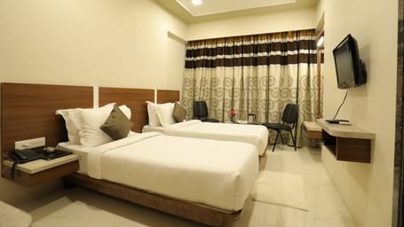 A Super Deluxe Room of Highland Resort furnished with twin beds, a wall-mounted TV, seating area for two, and closed curtains.