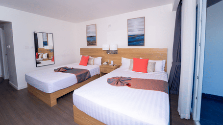 A Montego Bay hotel room with double beds, a wooden nightstand and an attached balcony at Hotel 39 Jamaica.