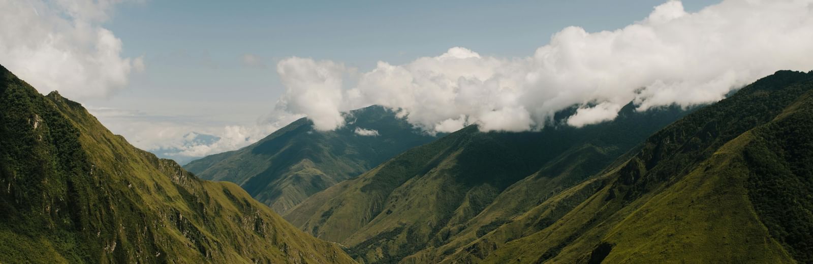 A verdant, steep-sided valley with a winding river below, under a cloudy sky.