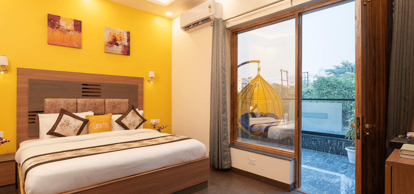 An image of a bedroom with a double size bed, a bedside table, and a glass slider door leading to the balcony - Lime Tree Hotel & One BHK, Noida Sector 50