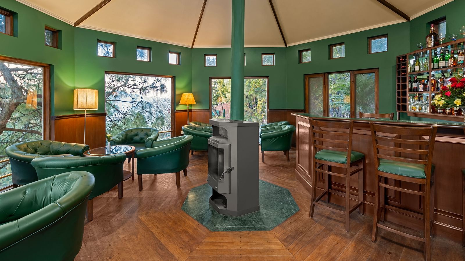 A bar featuring a wooden and green decor, with high chairs and sofas arranged comfortably with warm light lamps -  Baikunth resort, kasauli 