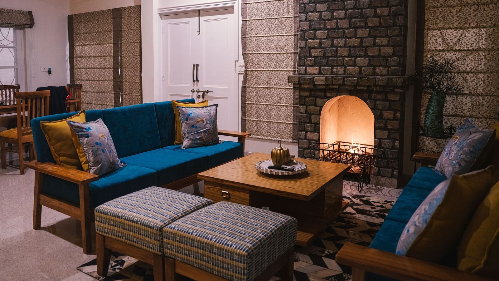 A living area with furniture arranged around a table by the fireplace at BluSalzz Villas - The Green Roof, Bhimtal.