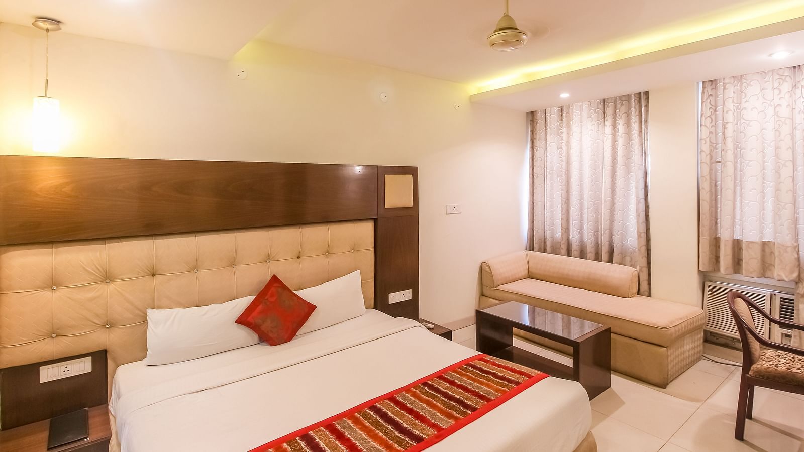 A cosy hotel room with a plush bed, a small sofa, and a glass-topped table. - Hotel Diamond Plaza, Chandigarh.