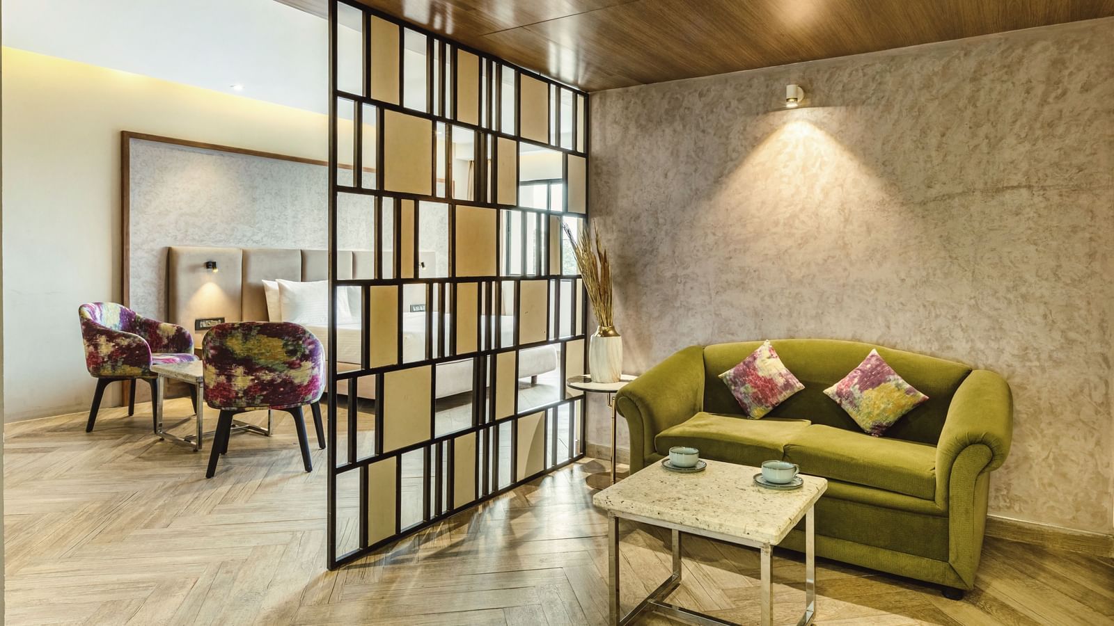 A seating area in a suite at Mango Hill Central, Chennai, with a green sofa and two purple chairs. A divider separates the seating from the rest of the room.