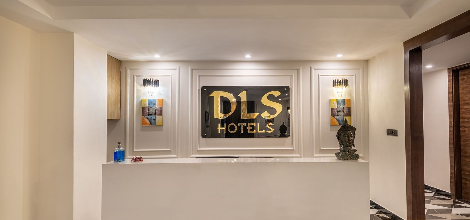 Image of the reception desk at DLS Grand Luxotica, Dehradun in warm lighting with a signage of DLS Hotels written on the wall behind the desk
