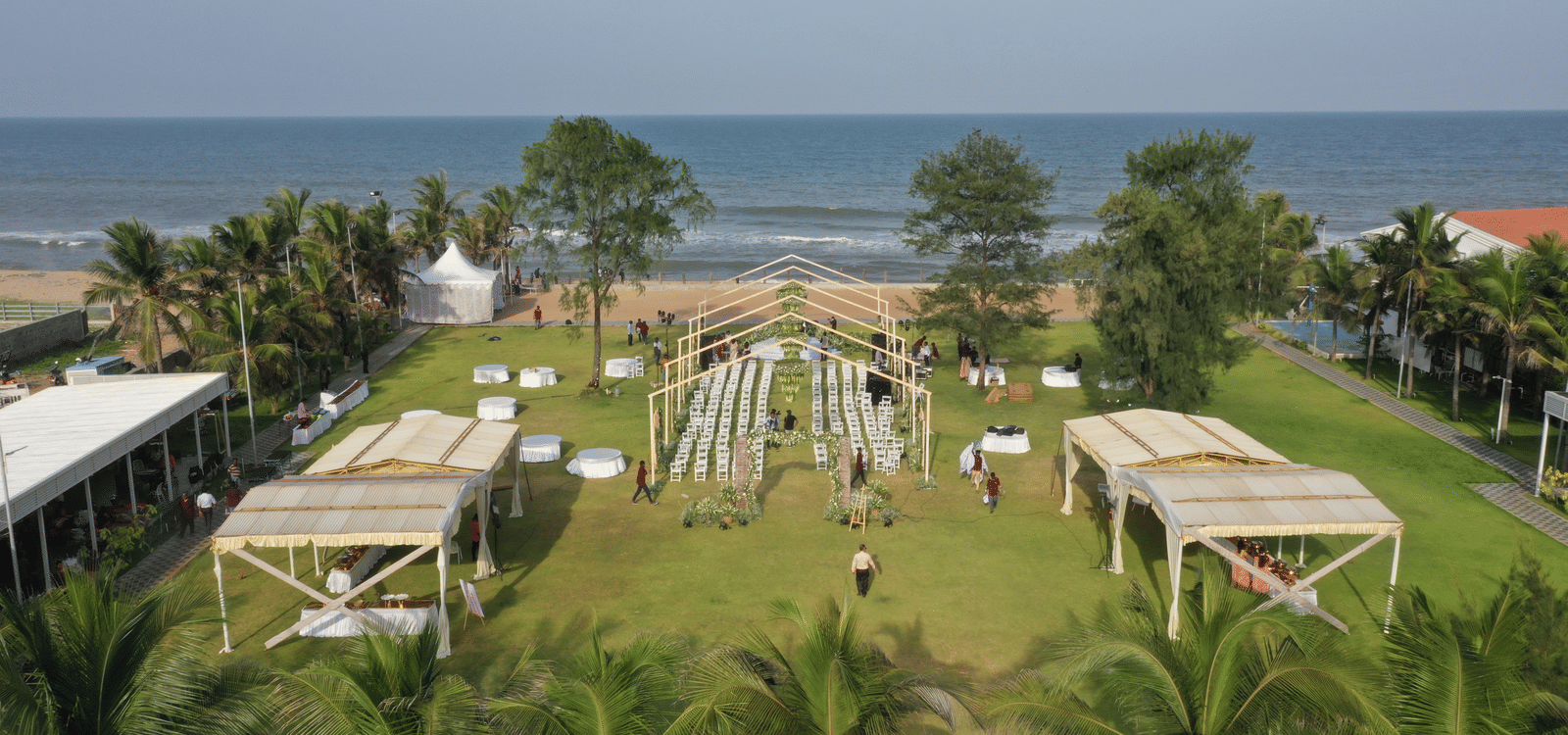 An aerial view of the lawn set up for a beach-side event, featuring shaded buffet counters, and a sea-facing seating area at Grande Bay Resort & Spa, Mamallapuram.
