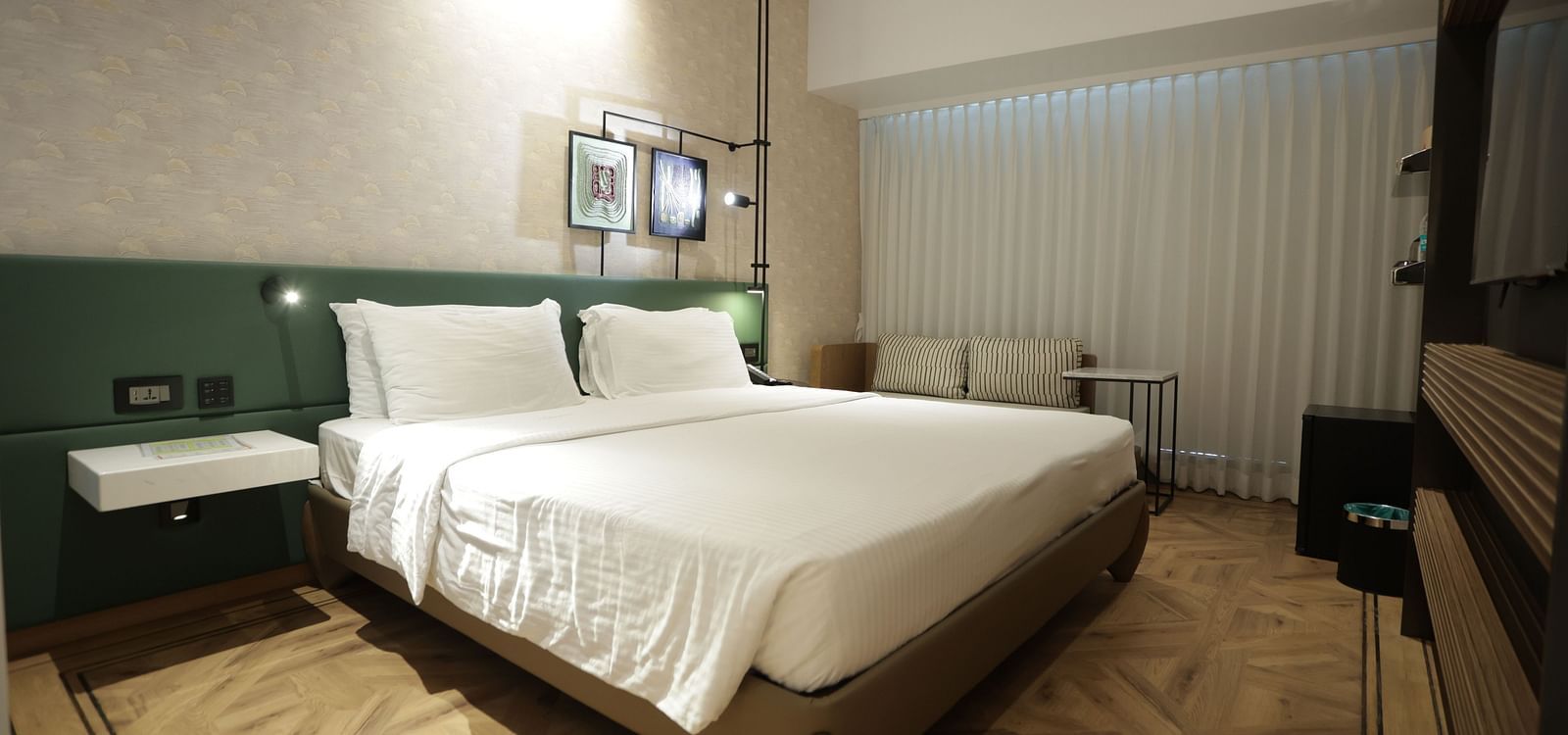 Modern guest room at Regency Hotel, Mumbai with plush bedding, contemporary furniture, large windows and elegant green accent wall for a comfortable stay.