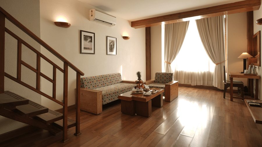 A duplex-style living area with a staircase, sofa seating, wooden flooring, and large windows allowing natural light in the Penthouse Suite at Clarks Amer, Jaipur.
