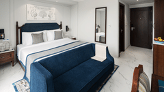 An image of a large bed with a blue bed runner, positioned in front of a work desk - MJ Sarovar Portico, Haridwar