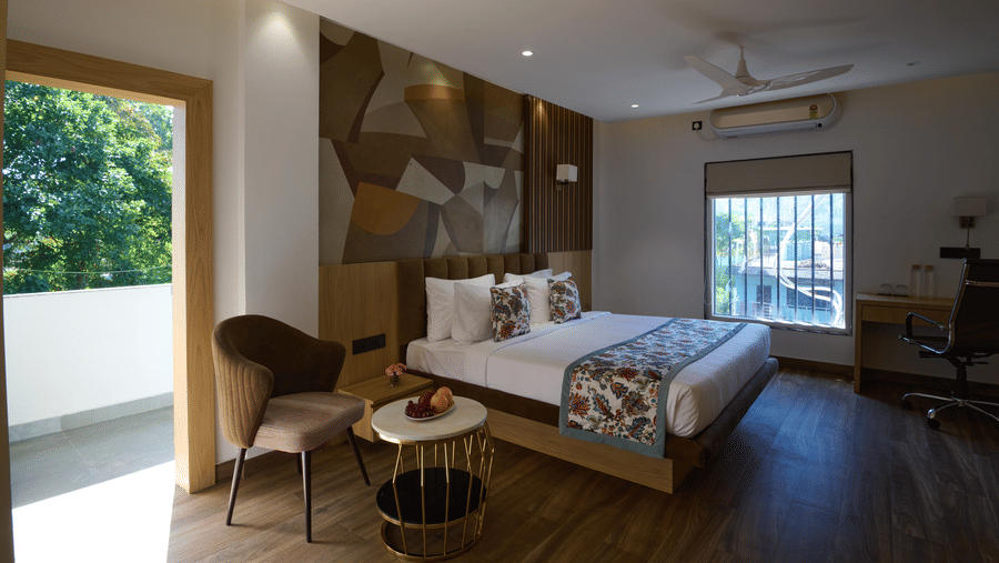 A spacious hotel room featuring a double bed, a patterned accent wall, a small table with chairs, and a sliding glass door to a balcony | Voyage Eastin Suites