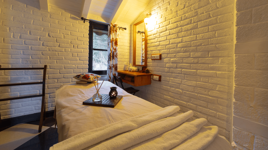 An intimate spa room with white brick walls, warm lighting, and a professional massage bed - Johnson Lodge & Spa, Manali