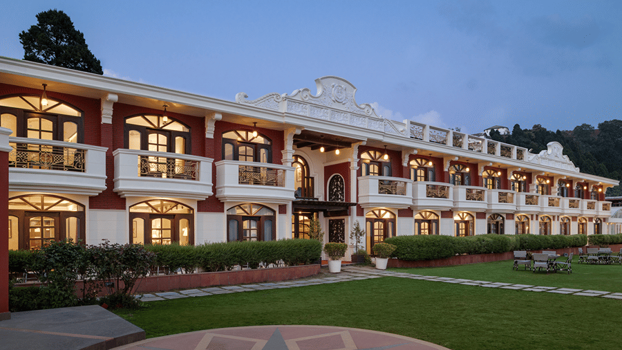 A long multi-story building facing an open lawn area under a blue sky at Ramada by Wyndham Mussoorie Mall Road.