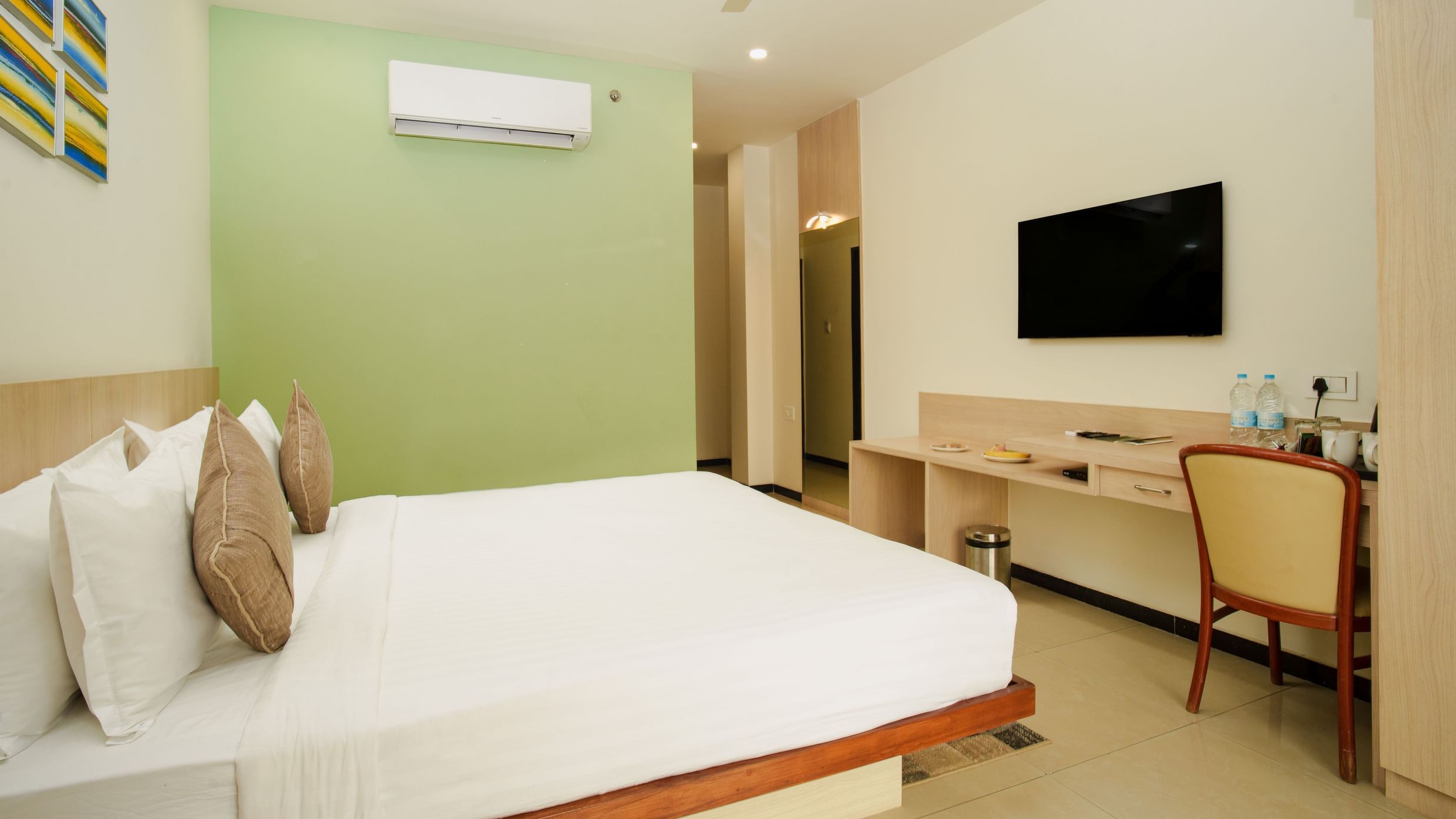 Hotel room with a large bed, desk, wall-mounted television, and a subtle green accent wall at Arawali Ananta Elite, Jaipur.
