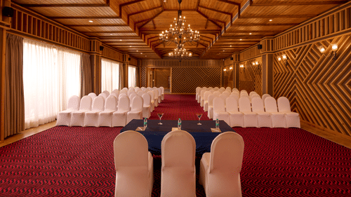 Empty banquet hall with wood-panelled walls, a sculpted ceiling with cove lighting, arched glass double doors, and a glossy tiled floor throughout.