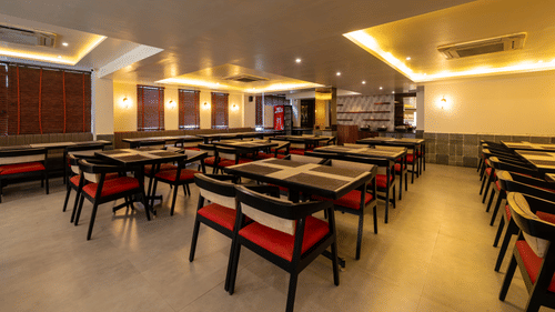 A wide-angled view of the clean dining hall at VITS Select, Bengaluru, with rows of tables, chairs, and soft cove lighting - one of the best restaurants in Hebbal.